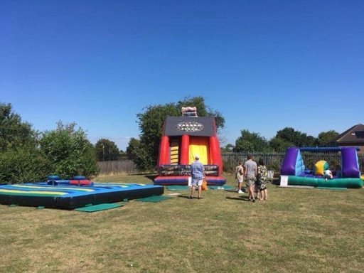 A bouncy castle, gladiator joust and inflatable assault course set up in a field